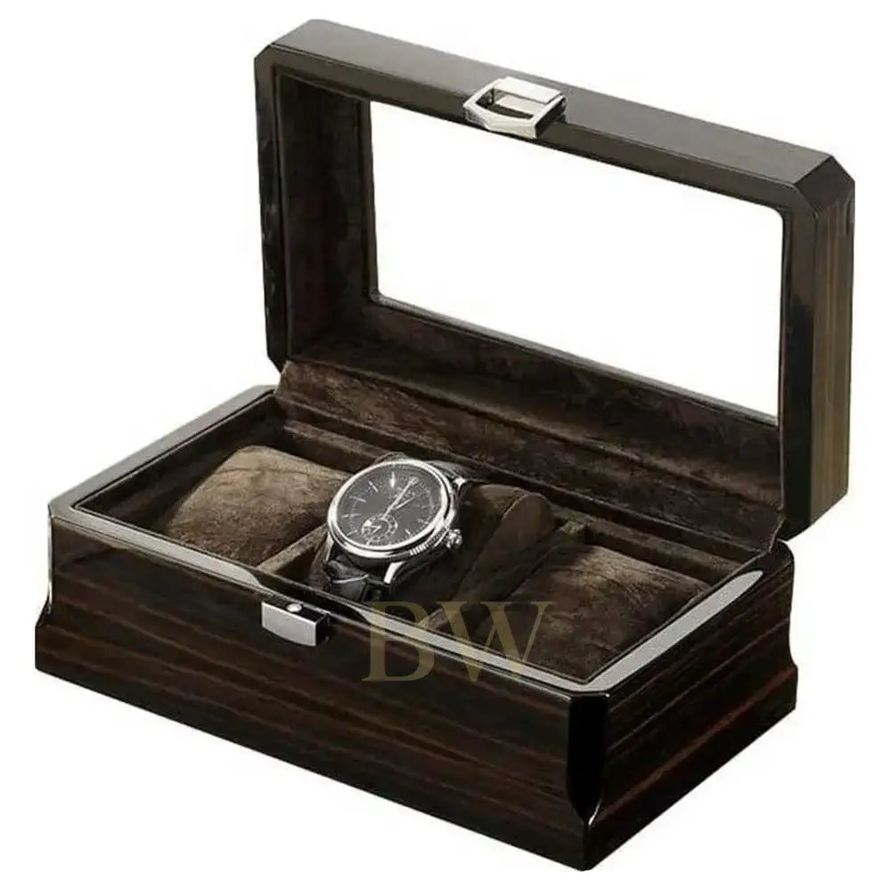 A luxury watch box with a dark wood grain exterior, a clear glass lid, and a plush dark brown velvet interior. A silver-tone chronograph watch with a black strap is displayed inside one of the three watch slots.