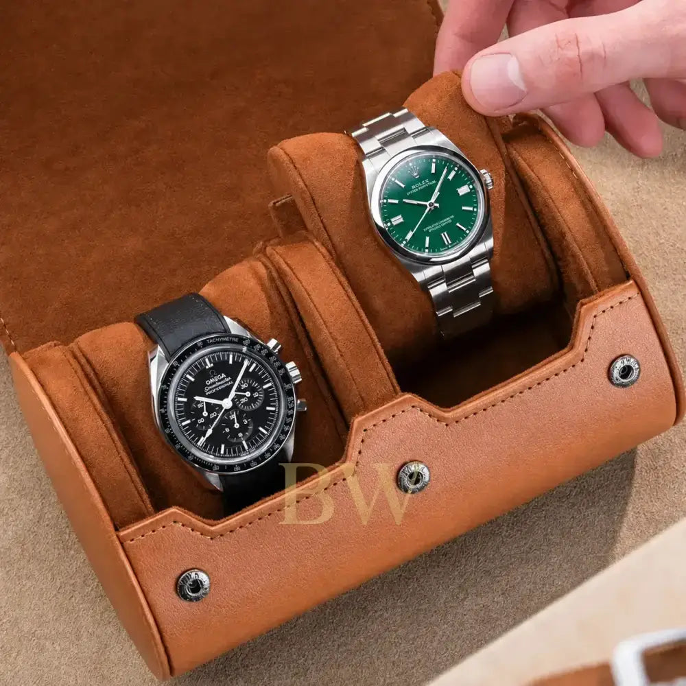 A tan leather watch roll with plush brown suede-like compartments holding two wristwatches, shown with a hand placing or adjusting the right watch. The product being sold appears to be the watch roll organizer rather than the watches themselves, since the rolls and exterior handle are prominently featured and the watches function as demonstration props.