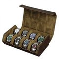 An open brown leather watch storage box with a brown suede-like interior, holding eight watches with silver bracelets and colorful dials.