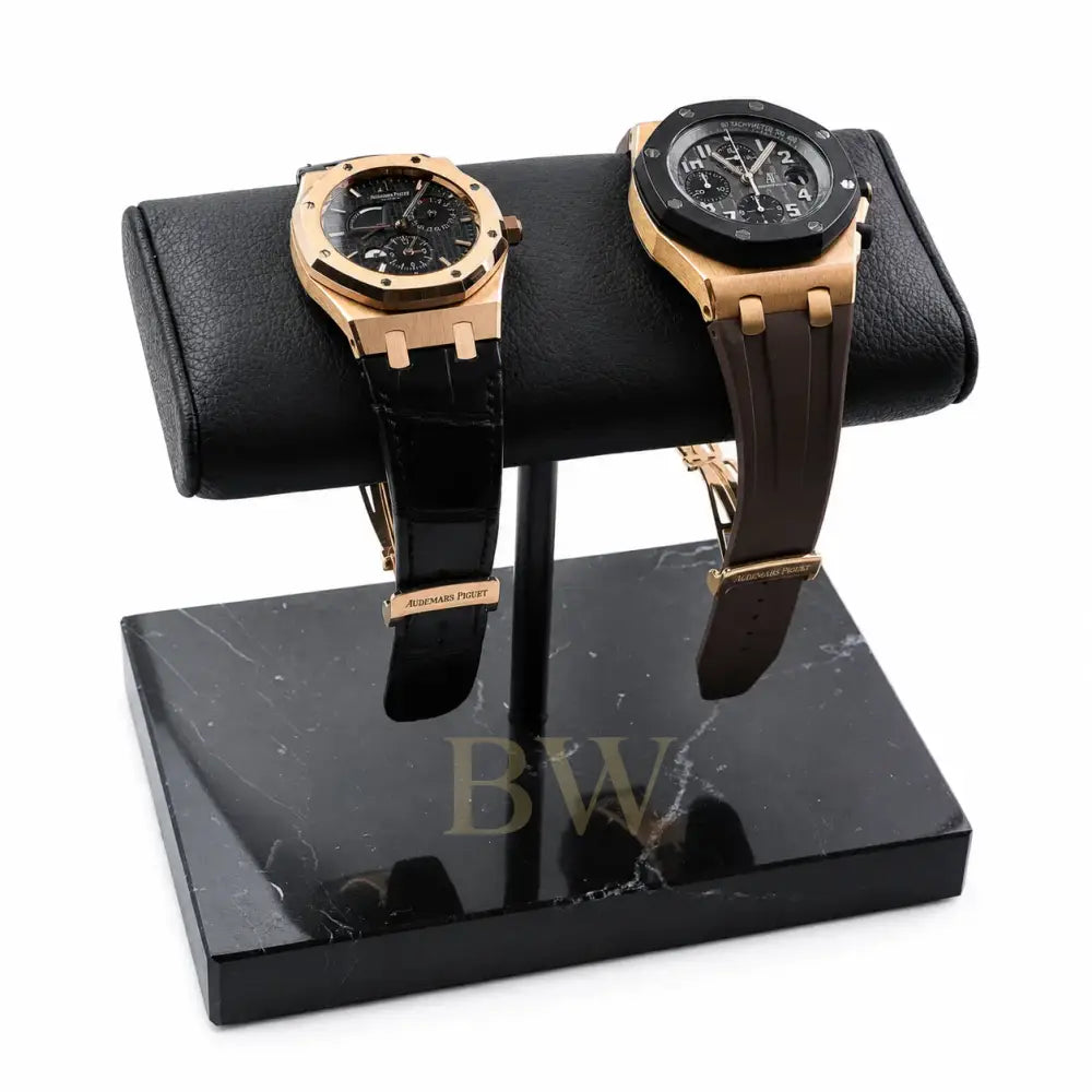 Two gold luxury watches Audemars Piguet on a black marble watch stand with a white background
