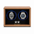 A wooden dual watch winder with a medium brown wood-grain finish, black textured interior, and two circular watch slots illuminated by blue LED lights. Two stainless Rolex and Audemars Piguet are displayed inside.