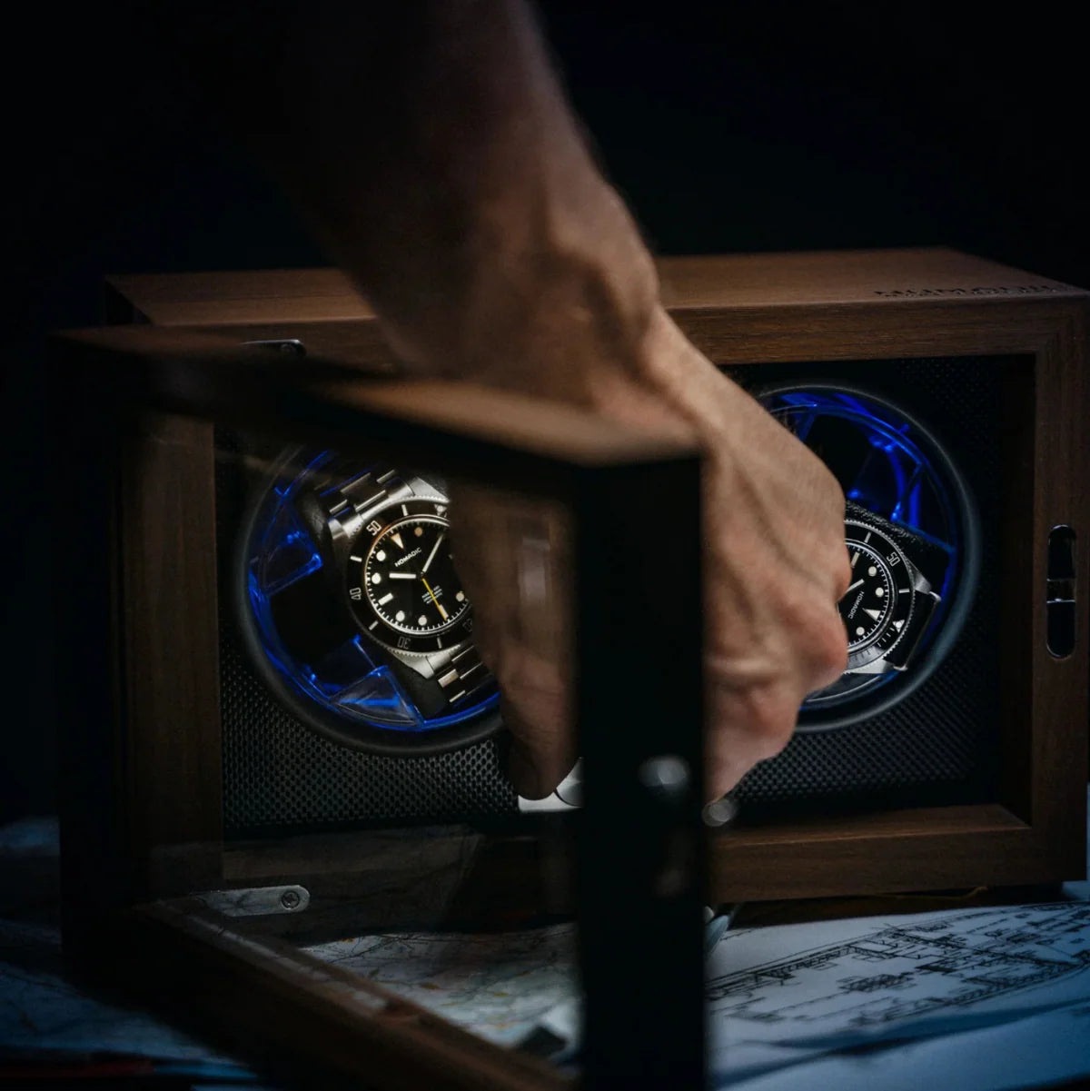 Hand opening a wooden watch winder with a watch inside, dark background