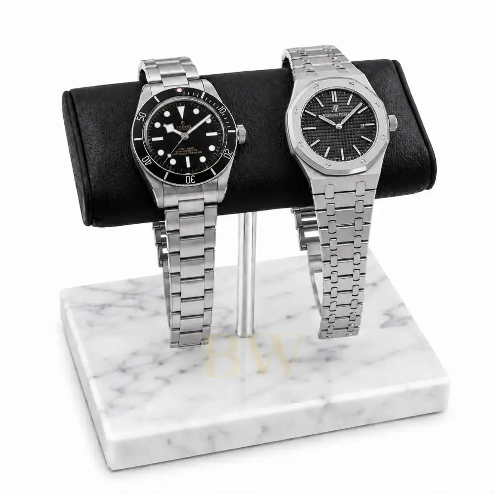 Two silver luxury watches Tudor and Audemars Piguet on a marble watch stand with a white background